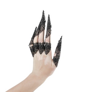 May include: A hand wearing a set of black, intricate, metal finger rings. The rings are designed to resemble claws or talons, with delicate, lacy details.