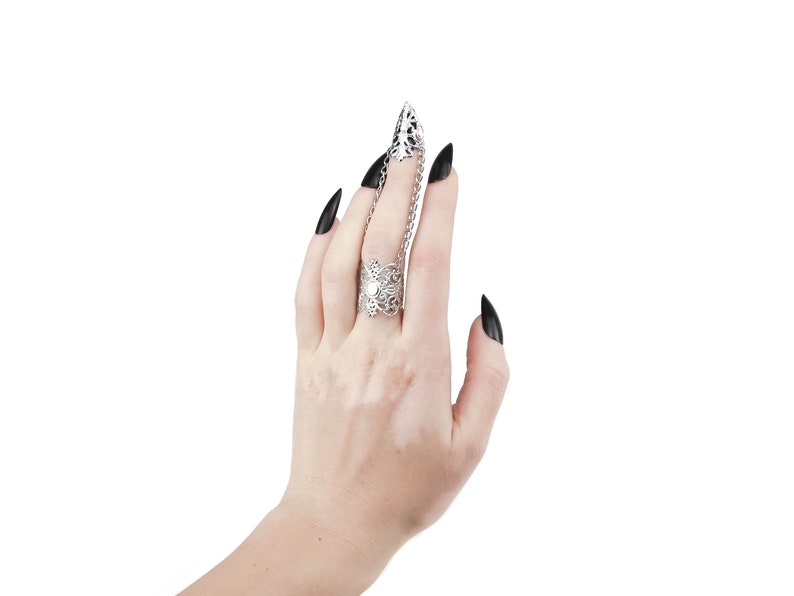 Puede incluir: Un anillo de plata con un delicado dise&ntilde;o floral y una cadena que se extiende hasta el dedo de al lado. El anillo se lleva en una mano con esmalte de u&ntilde;as negro.