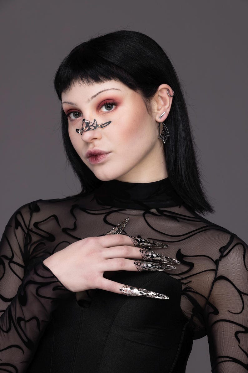 May include: A person wearing a black mesh top with silver claw-like rings on their fingers. The rings are detailed and intricate.