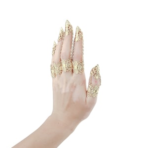 Puede incluir: Un conjunto de cinco anillos de dedo de tono dorado con intrincados dise&ntilde;os de filigrana. Los anillos est&aacute;n conectados por cadenas y presentan puntas puntiagudas.