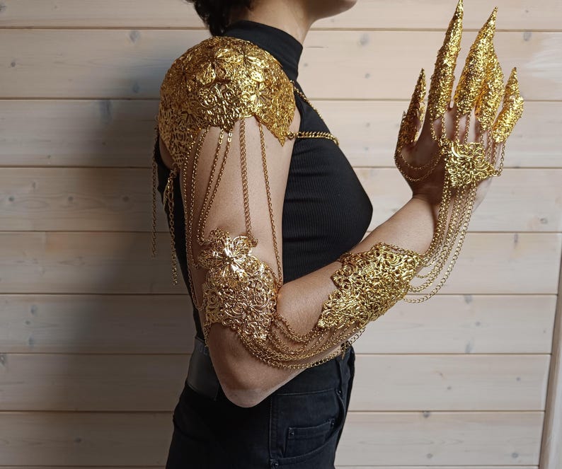 May include: Gold-toned arm and finger jewelry with intricate floral designs. The jewelry is made of metal and features chains and decorative elements.