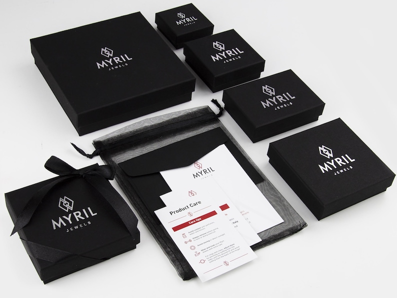 May include: Black jewelry boxes with the logo "Myril Jewels" printed in white. The boxes are arranged in a pyramid shape with a black mesh bag and a white card with product care instructions.