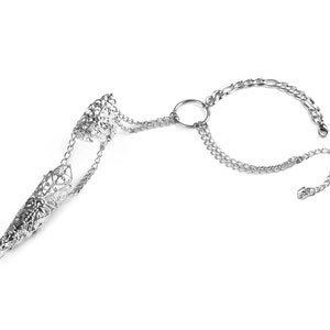 Pu&ograve; includere: Un anello in filigrana argentata con una lunga protezione per le dita a punta collegata a un braccialetto a catena. Il braccialetto ha una chiusura circolare e due maglie a catena.
