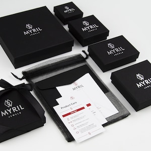 May include: Black jewelry boxes with the logo "Myril Jewels" on top. The boxes are arranged in a pyramid shape with a black mesh bag and a product care card in the center.