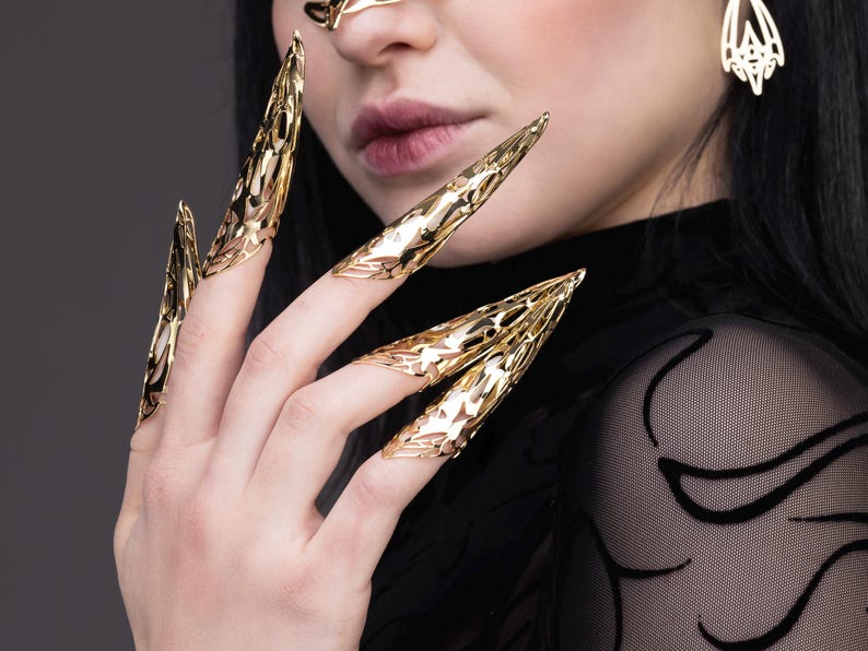 May include: Gold-toned claw-shaped rings worn on multiple fingers. The rings are intricate and detailed, resembling a sharp, pointed claw.