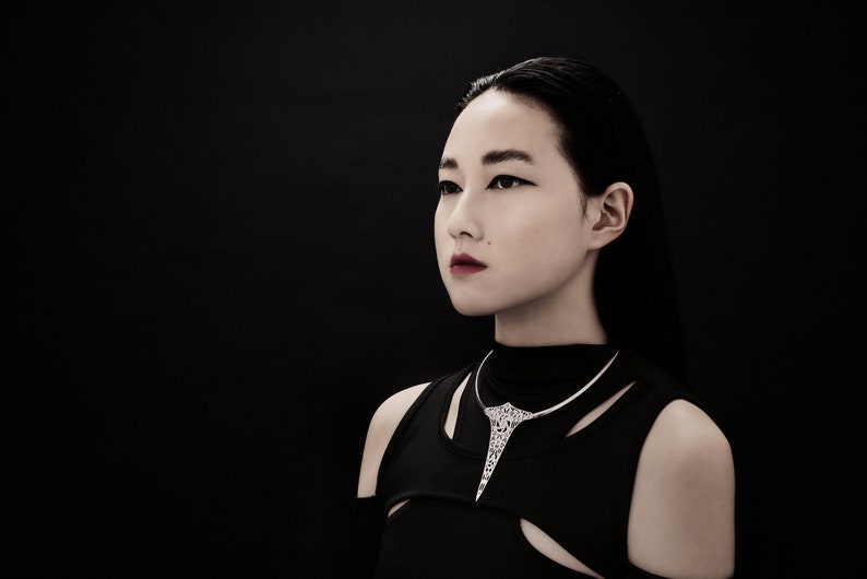 May include: A woman with long black hair wearing a black mock neck shirt and a silver necklace with a geometric design.