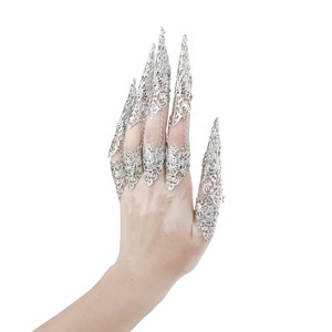 May include: A hand wearing silver filigree claw rings. The rings are intricate and detailed, with a pointed design.