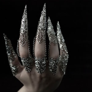 May include: A set of silver claw rings with intricate designs. The rings are connected by chains and are worn on multiple fingers.