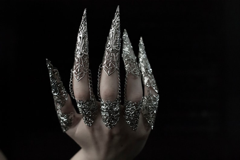 May include: A set of silver claw rings with intricate designs. The rings are connected by chains and are worn on multiple fingers.