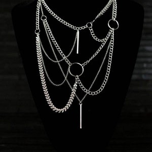 May include: A silver layered necklace with multiple chain styles, including a herringbone chain, and two pendant bars. The necklace features two circular rings.