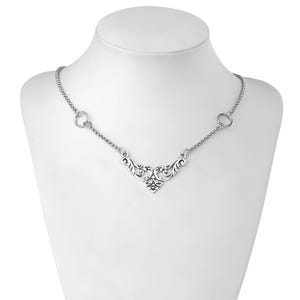 May include: A silver necklace with a delicate, ornate pendant featuring a floral design. The chain is made of small, linked circles.