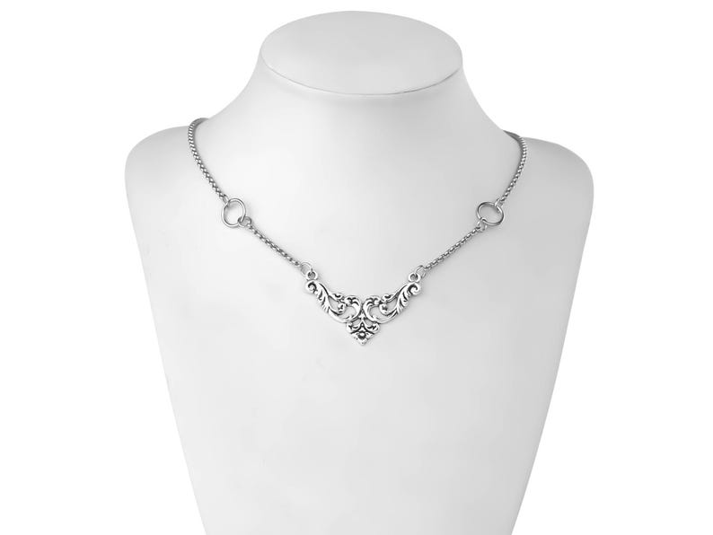 May include: A silver necklace with a delicate, ornate pendant featuring a floral design. The chain is made of small, linked circles.