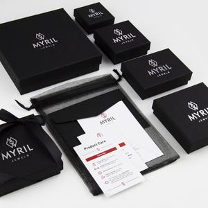 May include: Black jewelry boxes with the logo "Myril Jewels" printed in white. The boxes are arranged in a pyramid shape with a black mesh bag and a white card with product care instructions.