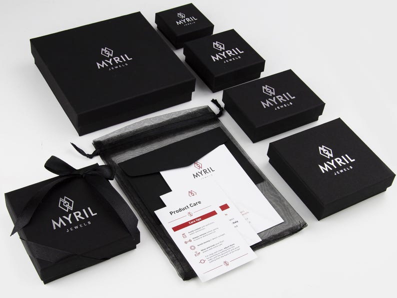 May include: Black jewelry boxes with the logo "Myril Jewels" printed in white. The boxes are arranged in a pyramid shape with a black mesh bag and a white card with product care instructions.
