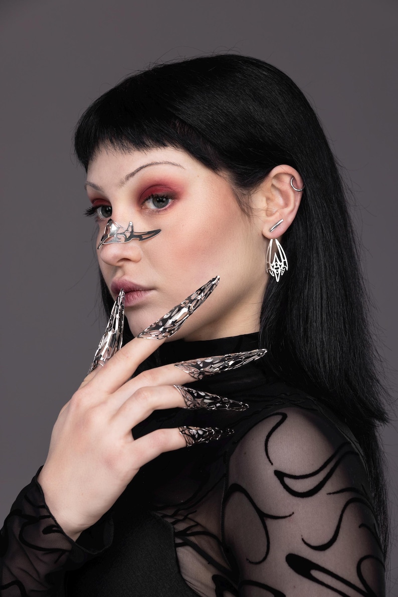 May include: A person wearing a black sheer top with a silver nose ring and silver rings on their fingers. The rings are shaped like claws.