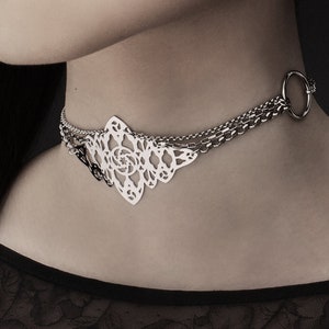 Puede incluir: Un collar gargantilla de plata con un diseño delicado e intrincado. El collar presenta múltiples cadenas y un gran colgante calado.