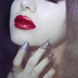 Puede incluir: Una mujer con el pelo largo y oscuro y un maquillaje dram&aacute;tico, lleva anillos de plata en los dedos. Los anillos tienen forma de garras puntiagudas con dise&ntilde;os intrincados.