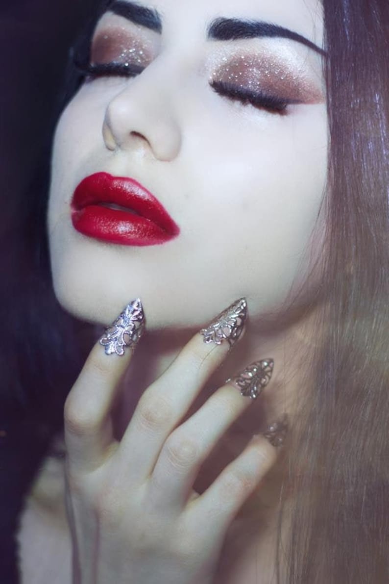 Puede incluir: Una mujer con el pelo largo y oscuro y un maquillaje dram&aacute;tico, lleva anillos de plata en los dedos. Los anillos tienen forma de garras puntiagudas con dise&ntilde;os intrincados.