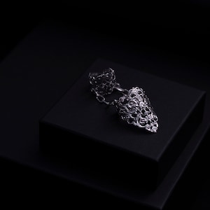 May include: A silver filigree ring with a pointed design. The ring is on a black velvet box.