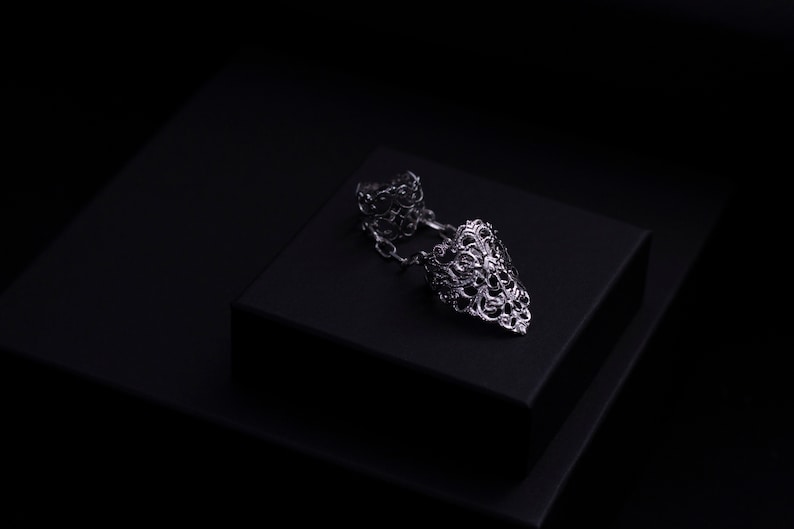 May include: A silver filigree ring with a pointed design. The ring is on a black velvet box.