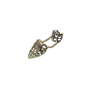 May include: A gold-toned filigree ring with a chain connecting to a pointed finger ring.