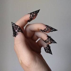 Puede incluir: Anillos de dedo de encaje negro con puntas puntiagudas. Los anillos se llevan en los dedos de una mano.