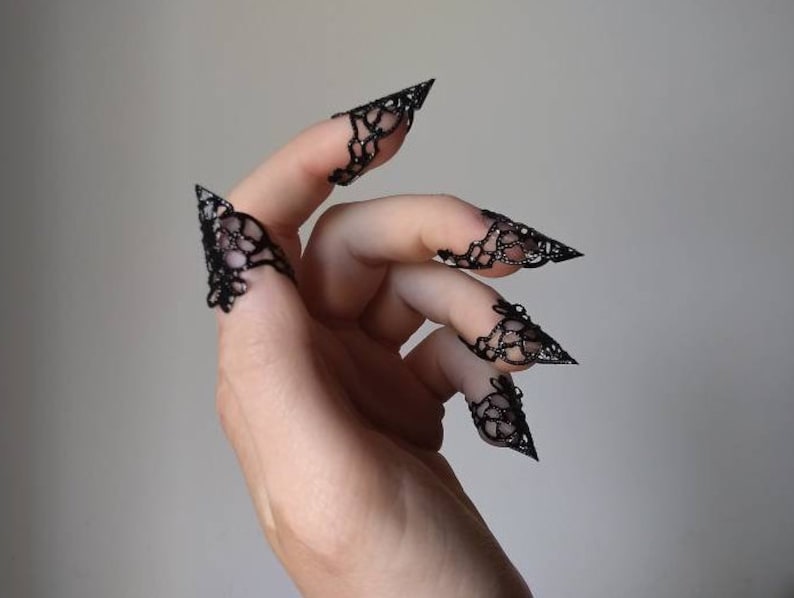 Puede incluir: Anillos de dedo de encaje negro con puntas puntiagudas. Los anillos se llevan en los dedos de una mano.