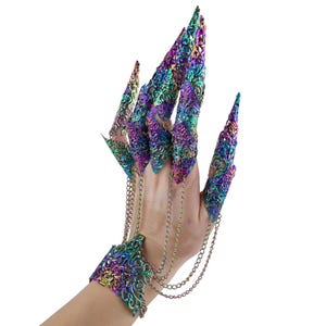 Può includere: Una mano ornata da un'armatura per le dita iridescente e da un braccialetto abbinato. L'armatura per le dita presenta lunghe estensioni appuntite collegate da delicate catene. I gioielli mostrano un mix di tonalità viola, verdi e blu.