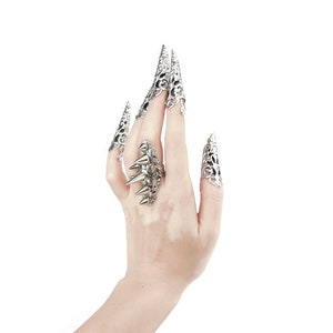 Pu&ograve; includere: Una mano che indossa diversi anelli d'argento con disegni intricati. Gli anelli sono sull'indice, il medio e l'anulare. Gli anelli hanno la forma di artigli.