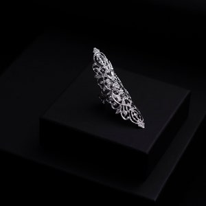 Op de afbeelding: Een zilveren ring met een delicaat, ingewikkeld ontwerp. De ring ligt op een zwarte displaystandaard.