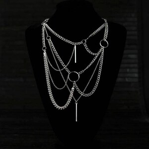 May include: A silver layered chain necklace with multiple chain styles and circular and bar pendant accents.