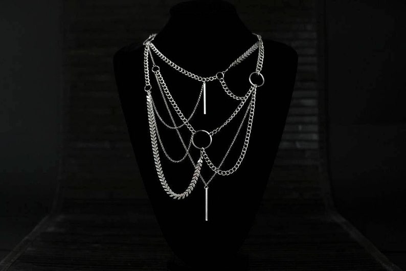 May include: A silver layered chain necklace with multiple chain styles and circular and bar pendant accents.