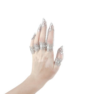 Puede incluir: Una mano con anillos de garra de filigrana plateada. Los anillos est&aacute;n conectados por cadenas y tienen un dise&ntilde;o delicado e intrincado.