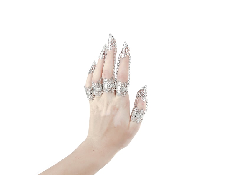 Puede incluir: Una mano con anillos de garra de filigrana plateada. Los anillos est&aacute;n conectados por cadenas y tienen un dise&ntilde;o delicado e intrincado.