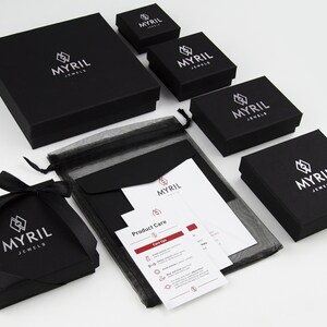 Assortment of Myril Jewels brand packaging, featuring elegant black boxes of various sizes with the company's logo in silver, along with care instructions and black organza gift bag