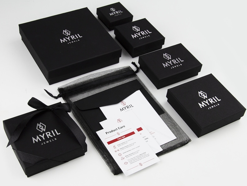 Assortment of Myril Jewels brand packaging, featuring elegant black boxes of various sizes with the company's logo in silver, along with care instructions and black organza gift bag