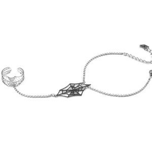 May include: A silver chain bracelet with a black spiderweb charm and a matching ring. The bracelet has a lobster clasp closure.