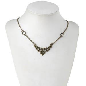 May include: A gold-toned necklace with a delicate, ornate pendant in the shape of a stylized heart. The chain is thin and has a simple design.