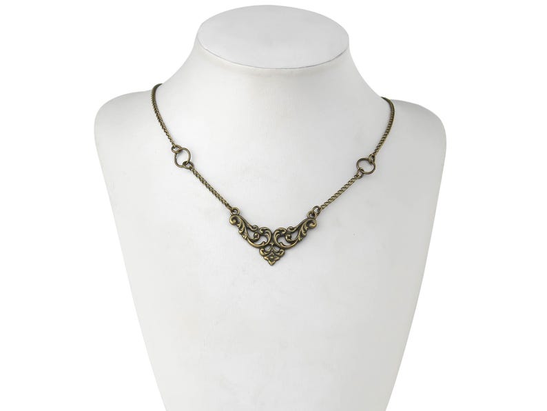 May include: A gold-toned necklace with a delicate, ornate pendant in the shape of a stylized heart. The chain is thin and has a simple design.