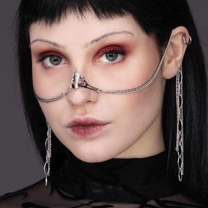 Könnte beinhalten: Eine silberne Nasenkette mit einem dekorativen Nasenteil. Die Kette ist mit einem silbernen Ohrclip mit einer baumelnden Kette verbunden.