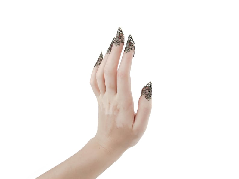 Puede incluir: Una mano con cinco anillos de dedo decorativos con un dise&ntilde;o de filigrana. Los anillos son de metal y tienen un acabado bronce oscuro.