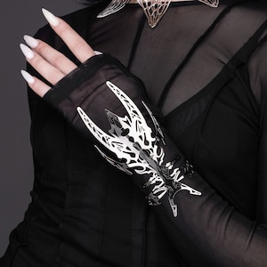 Peut inclure: Gants sans doigts en maille noire transparente avec un motif décoratif en métal argenté sur le dos de la main. Le motif est complexe et présente un motif géométrique.