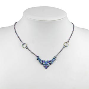 May include: A silver necklace with a delicate iridescent floral design pendant and two circular accents. The necklace is on a white mannequin.