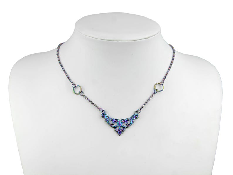 May include: A silver necklace with a delicate iridescent floral design pendant and two circular accents. The necklace is on a white mannequin.