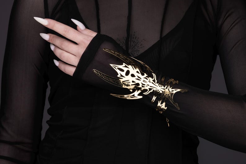 Puede incluir: Una camisa negra de manga larga de tul con un dise&ntilde;o met&aacute;lico dorado en la manga. El dise&ntilde;o es intrincado y se asemeja a un drag&oacute;n estilizado.