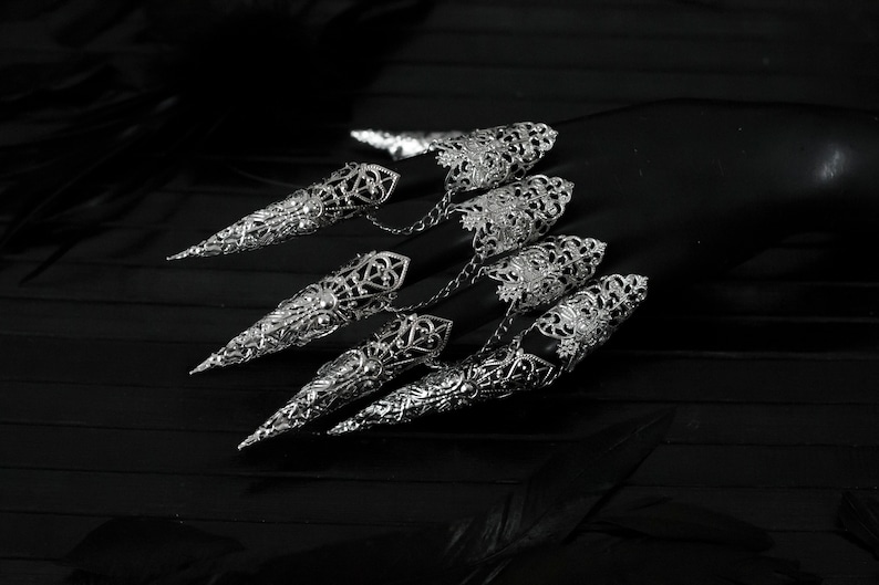 May include: A set of silver filigree knuckle rings with pointed tips, designed to be worn on multiple fingers.