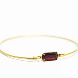 Puede incluir: Un brazalete de oro con una sola piedra rectangular roja.