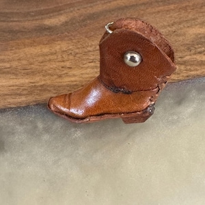 May include: A small brown leather cowboy boot keychain with a silver metal ring and a silver button.