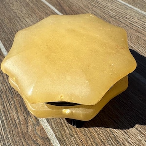 May include: A yellow, star-shaped, decorative object with a smooth, textured surface. The object is made of two layers and has a black base.