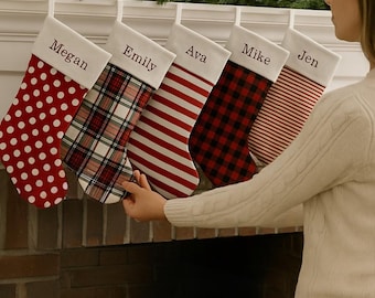 May include: Five personalized Christmas stockings hanging in a row. The stockings feature different patterns: red with white polka dots, red and black plaid, red and white horizontal stripes, red and black buffalo check, and red and white thin stripes.